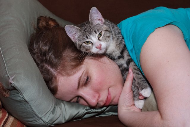 Julia Miller lying on the couch while Sasha lies on top of her, looking peeved.