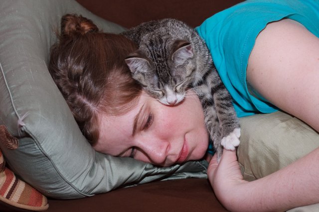 Julia Miller lying on the couch while Sasha lies on top of her, looking peeved.